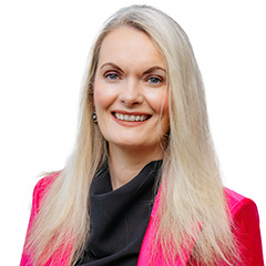 Lorraine Walsh has blone hair, blue eyes, and is smiling. She is wearing a black top which is covered by a bright pink blazer.
