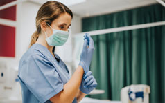 A female medical professional wearing a surgical mask and putting on gloves.
