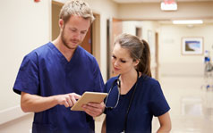 A female and male medical professionals in a hospital looking at a tablet together.