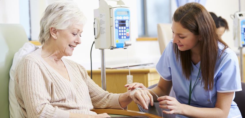 A nurse assists an elderly woman in a hospital setting, providing care and support during her chemotherapy treatment