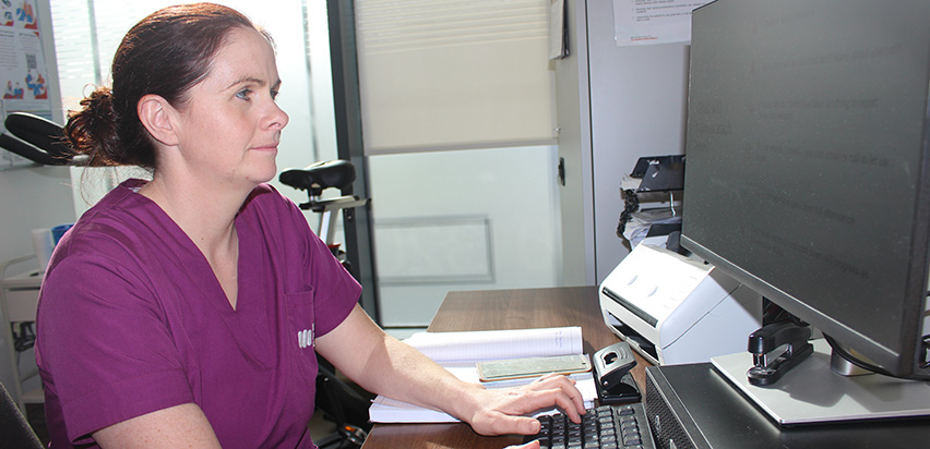 Irene Murphy is wearing a purple top and is sitting in front of a computer. She is looking at the screen a typing on a keyboard.