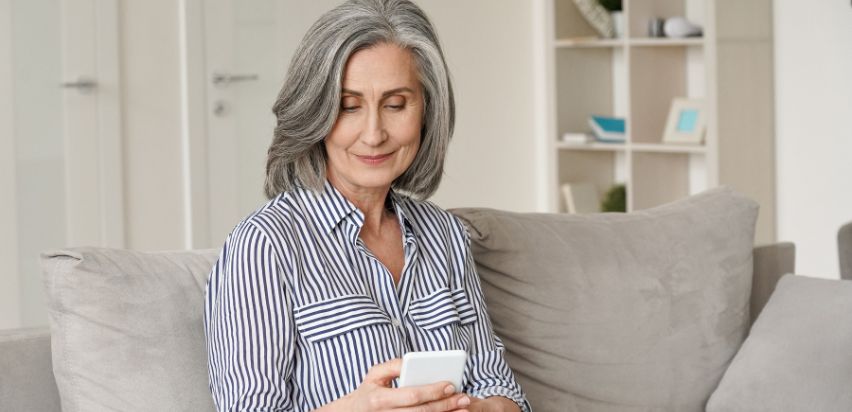 A woman sitting on a couch in her living room looking at her phone.