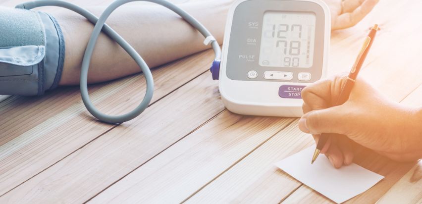 A doctor writing down a patient's blood pressure monitor reading.