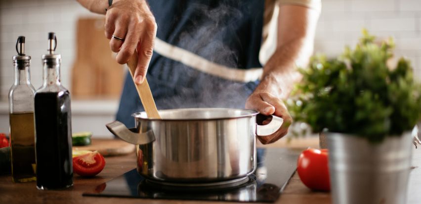 A man stirring a steaming pot in a kitchen. 