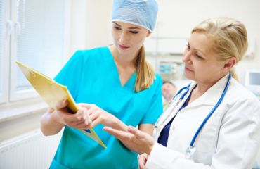 Nurse and doctor in a hospital setting reviewing patient information on a clipboard.