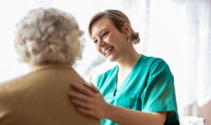 A female medical professional is smiling at an older woman and has her hand on the woman's back.