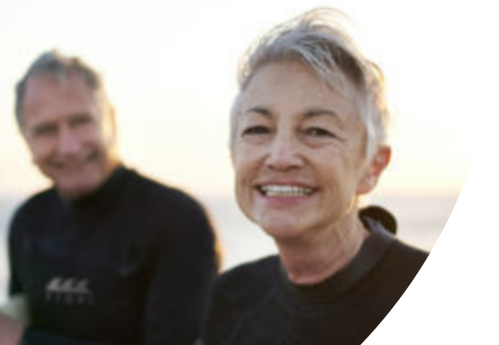 A man and a woman standing on a beach are smiling and holding surf boards.
