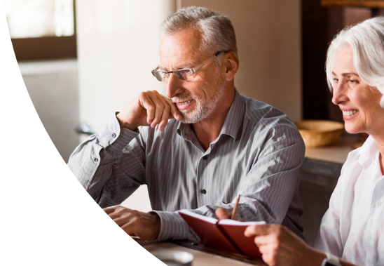 A married couple looking at a computer together. The wife is taking notes in her notebook.